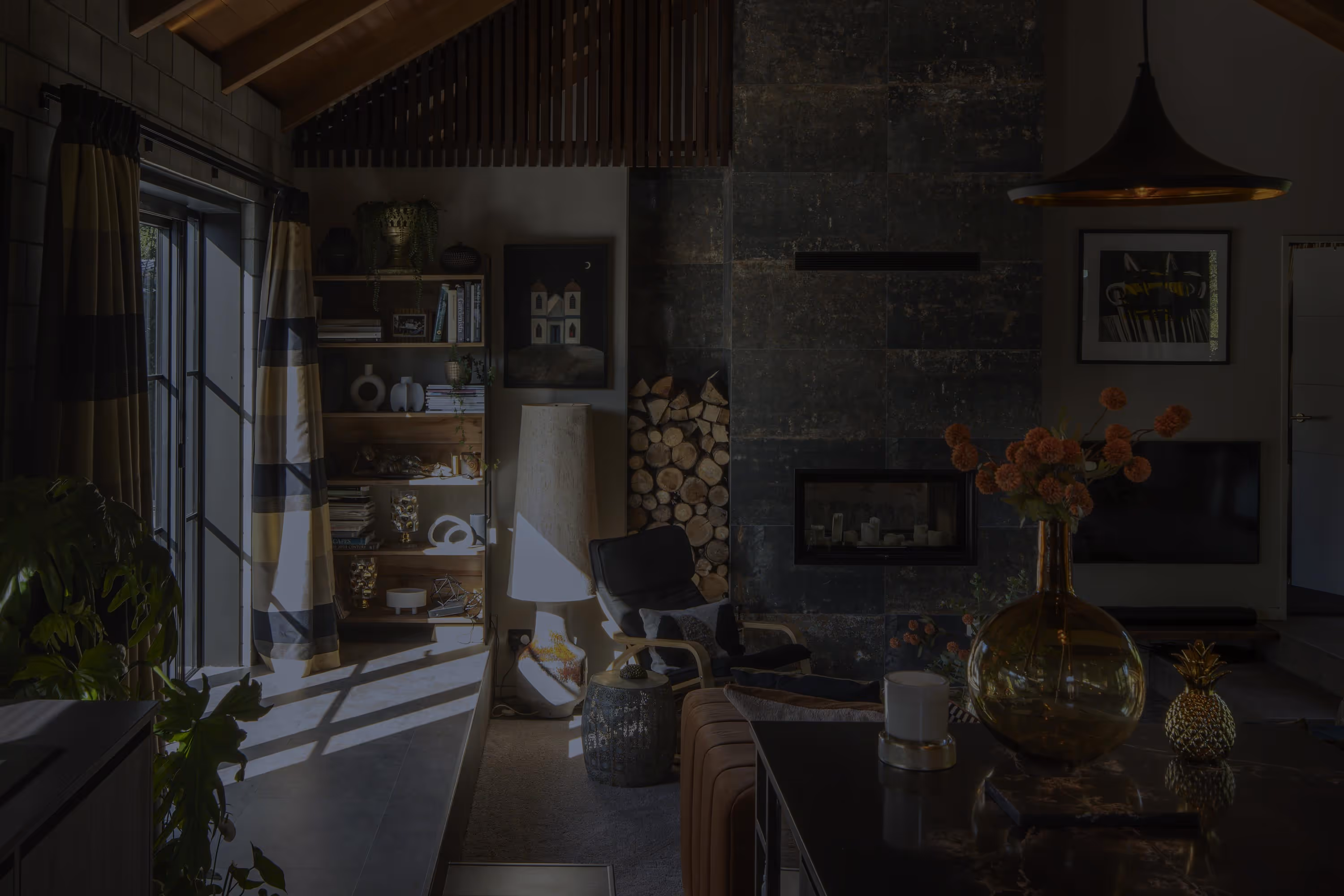 Living room at the Smith House in Greytown with vaulted timber ceiling, stone fireplace, large windows, and dark marble kitchen island.