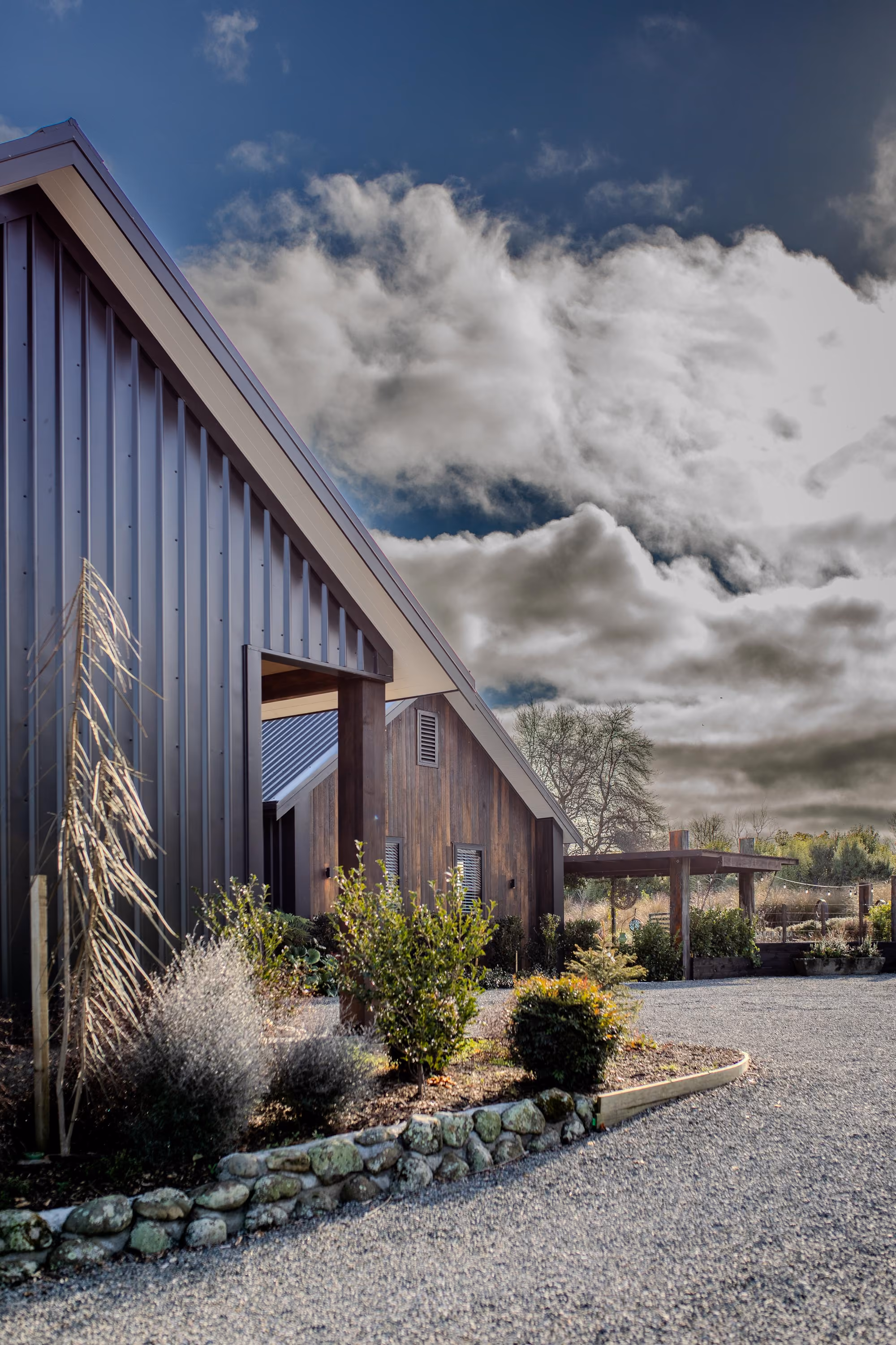 Exterior gable end of the home with dark vertical cladding and landscaped garden beds