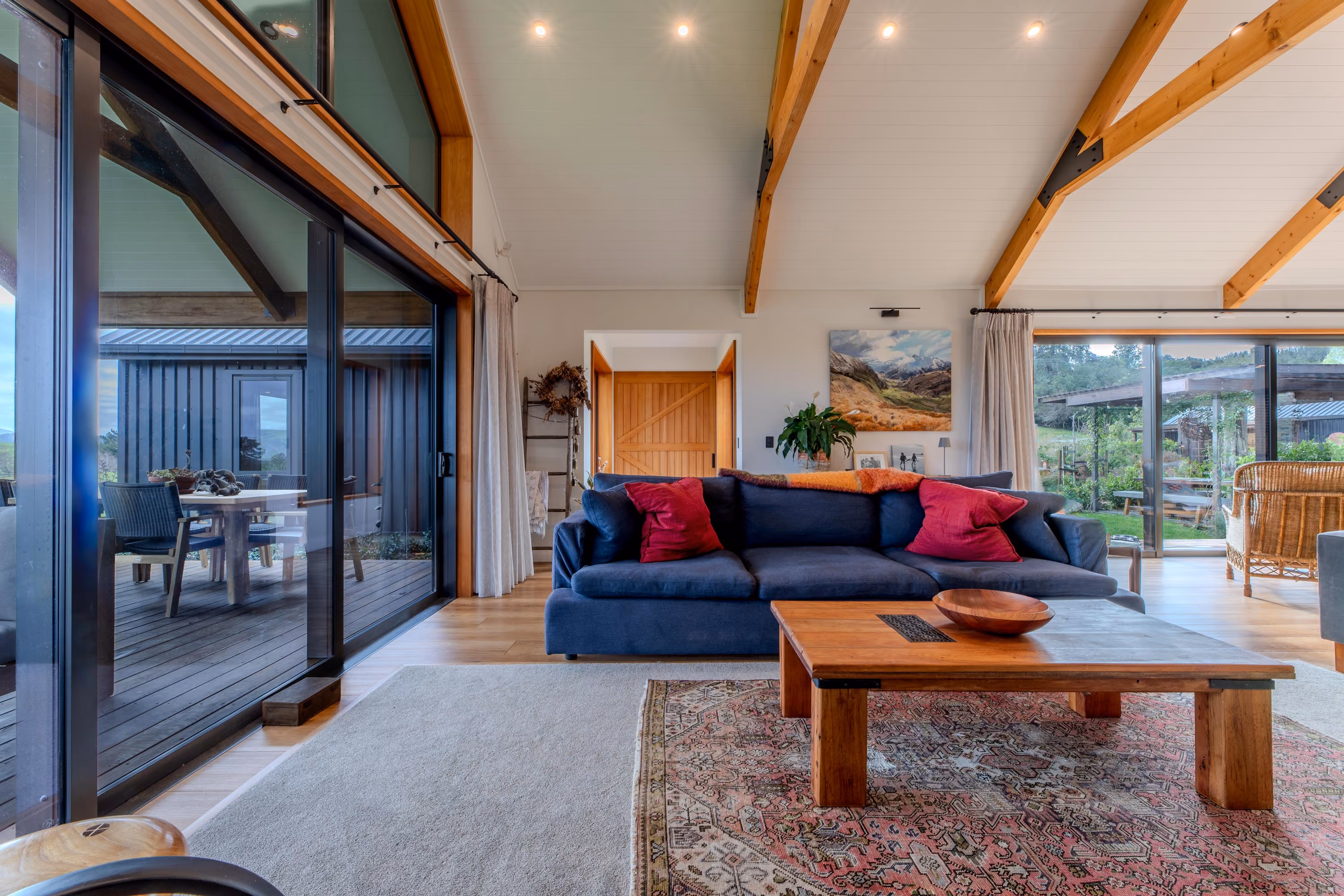Living room with vaulted timber-beamed ceiling, glass sliding doors and a navy sofa on a patterned rug