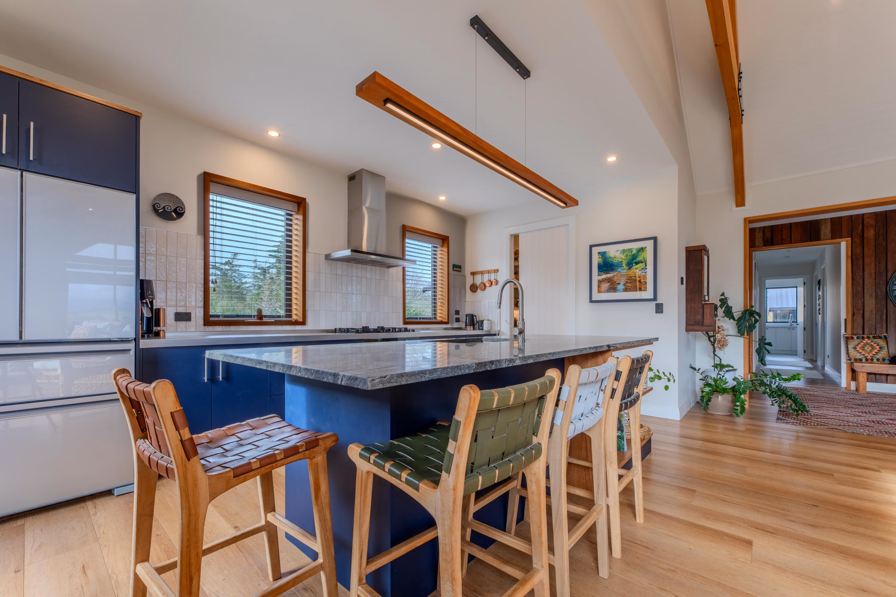 Kitchen with navy blue island bench, timber bar stools and pendant lighting over timber flooring