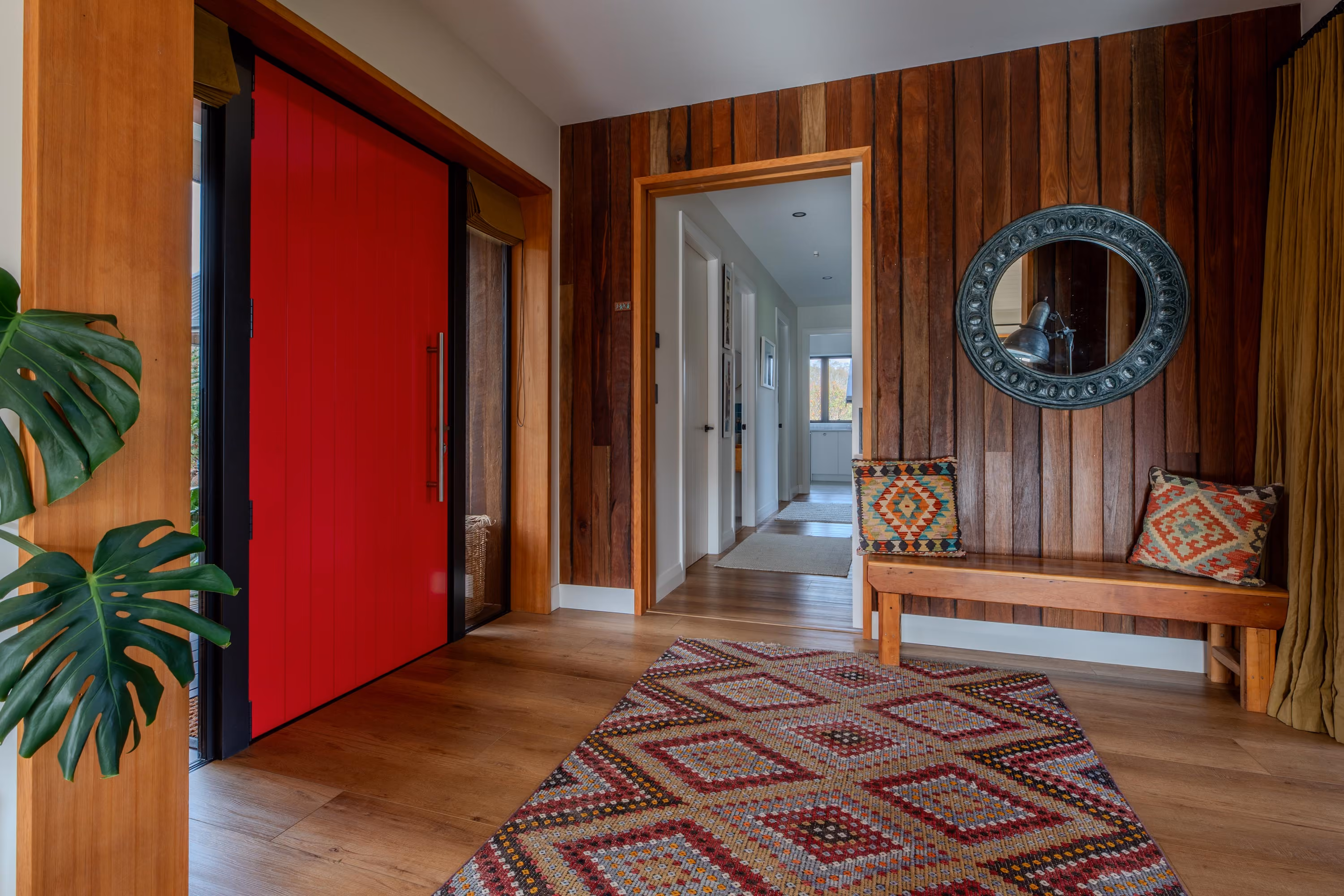 Entrance hallway with a red barn door, timber wall panelling, round mirror and patterned rug