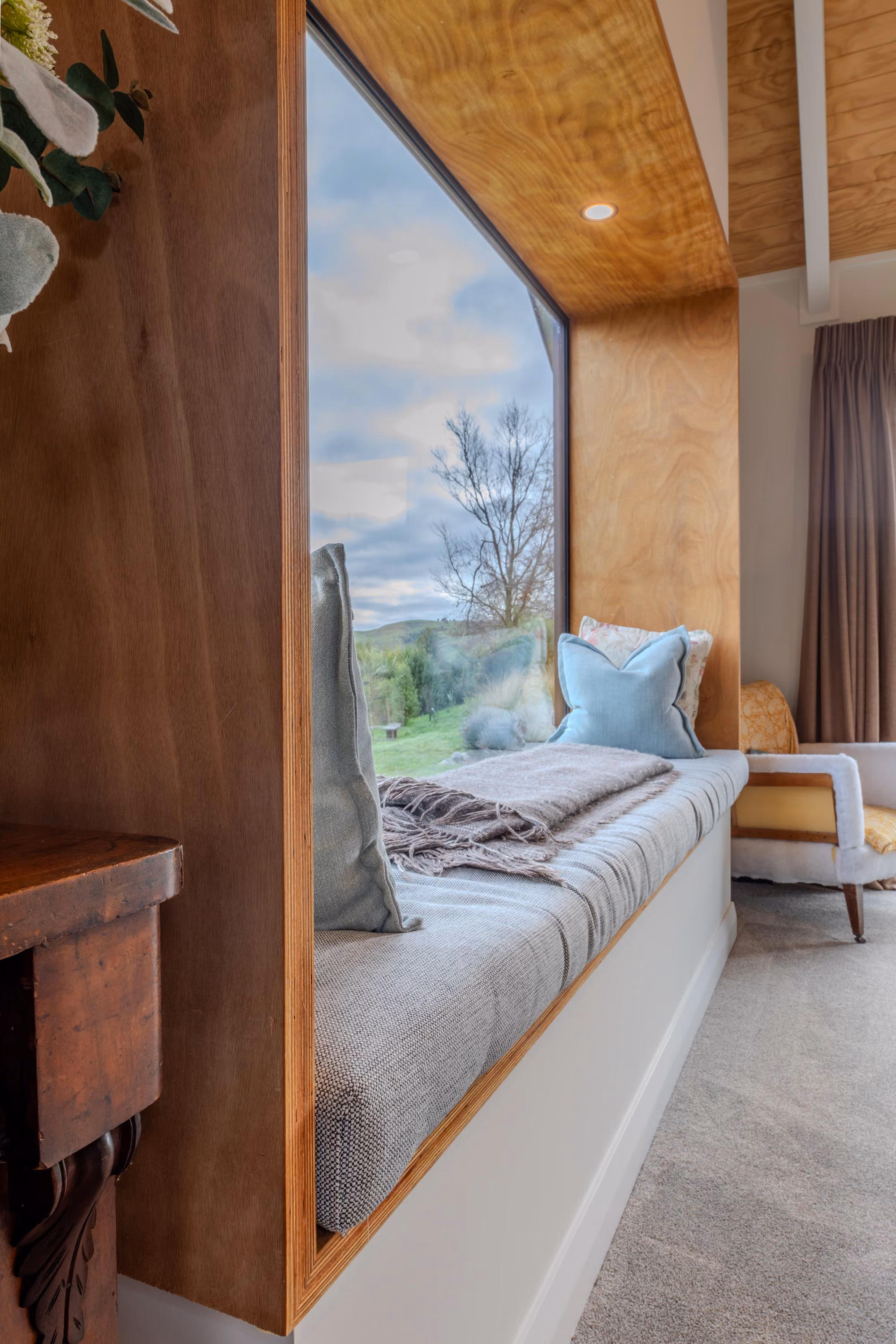 Built-in window seat with cushions beneath a timber-lined ceiling and window