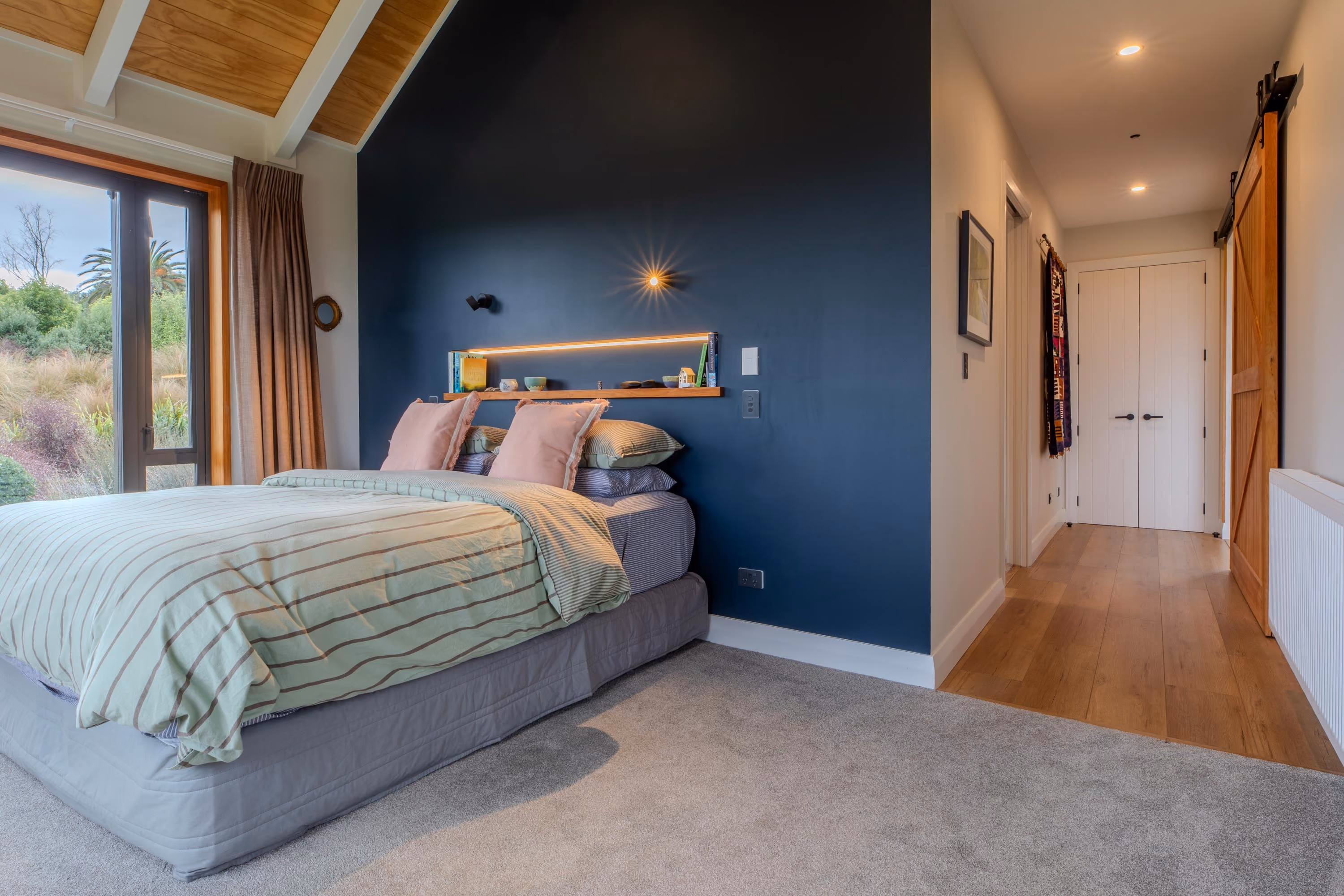 Bedroom with a navy accent wall, timber ceiling, striped bedding and a sliding barn door