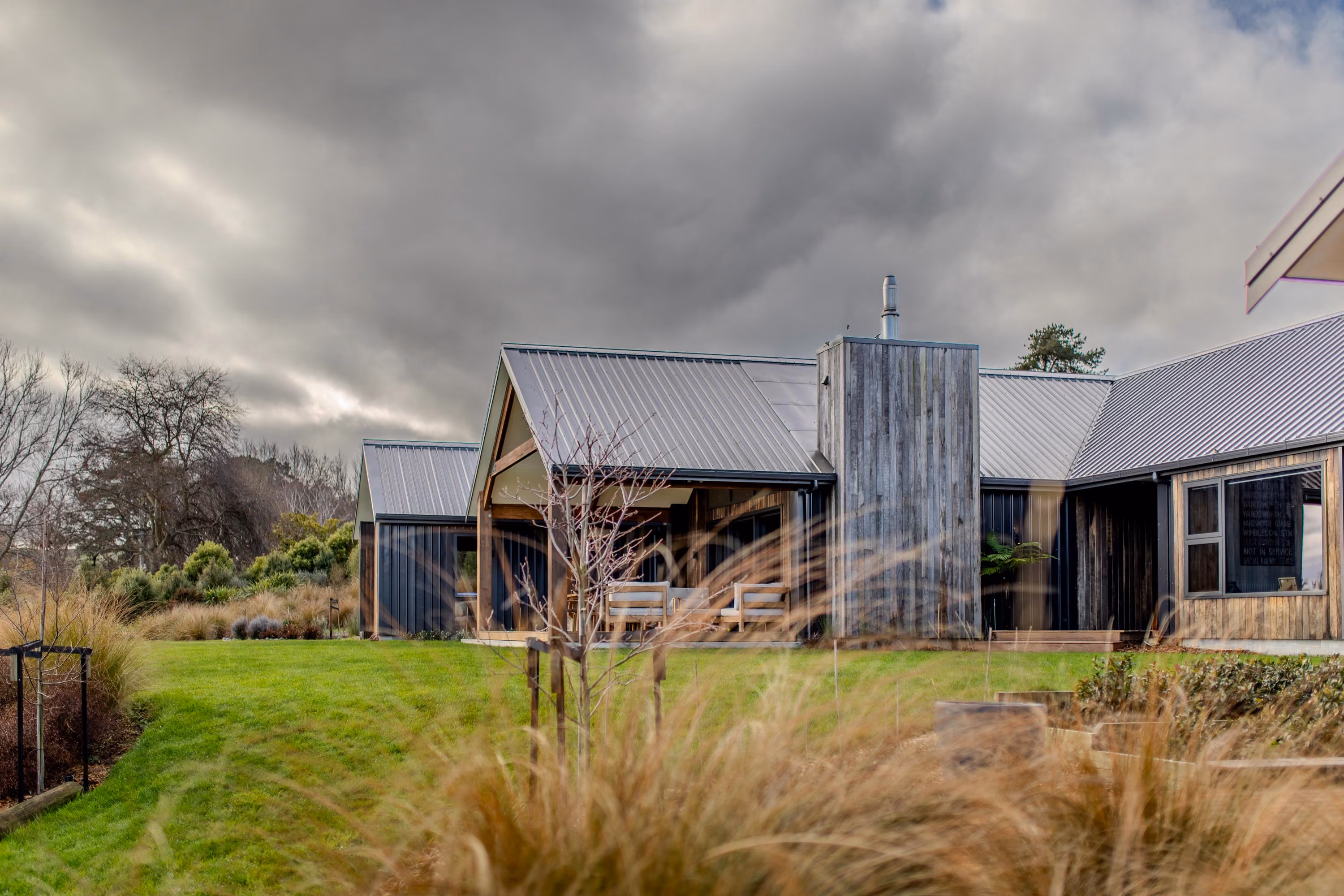 Exterior view of the home under a cloudy sky, showing weatherboard cladding, chimney and lawn