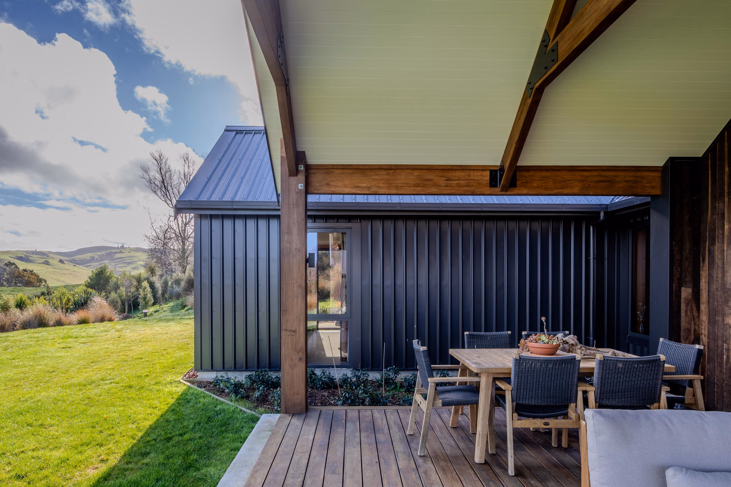 Covered outdoor dining area with timber table and chairs, overlooking rolling green hills