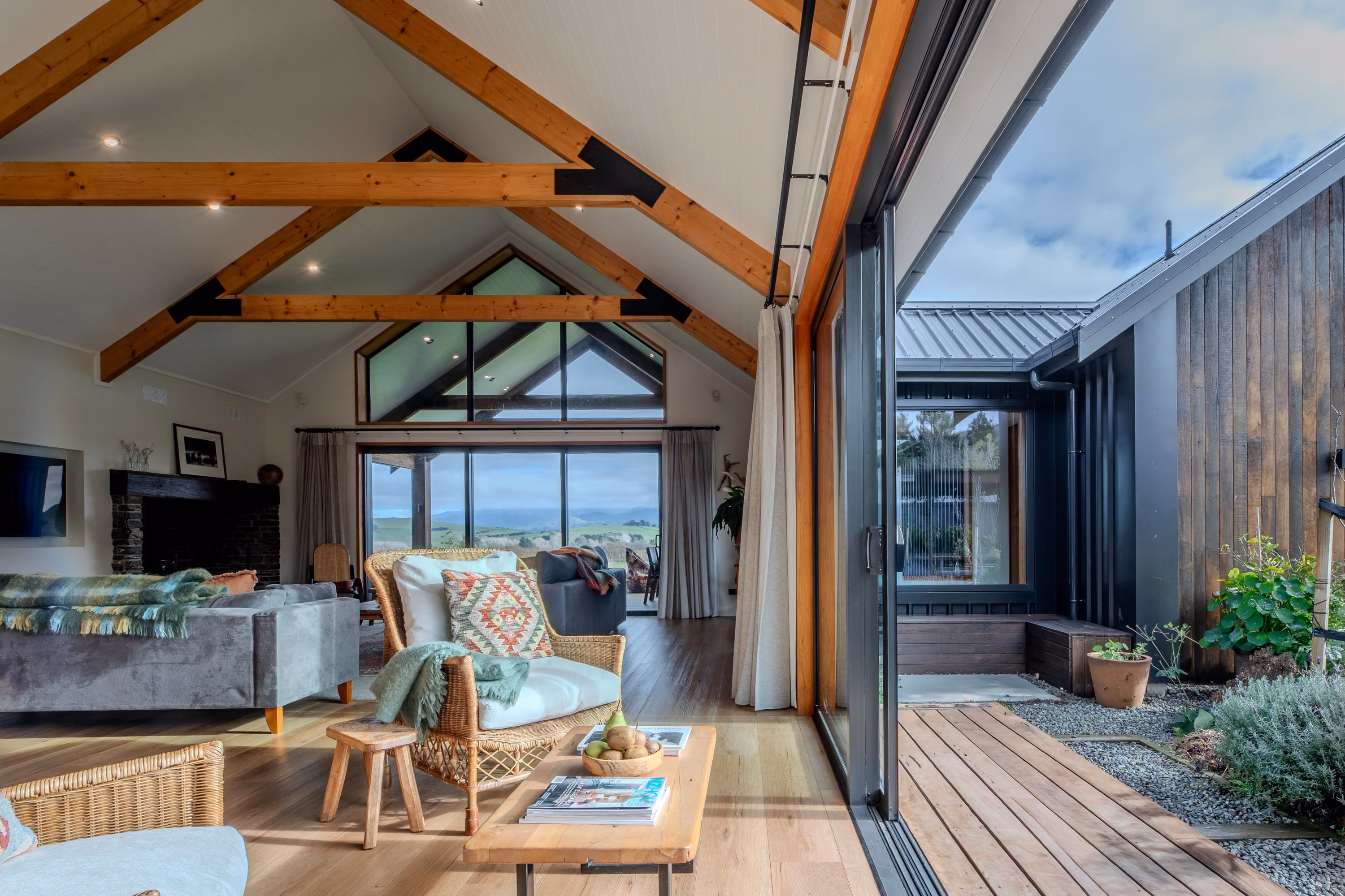 Open-plan living space with vaulted timber-beamed ceiling and sliding glass doors opening onto a deck