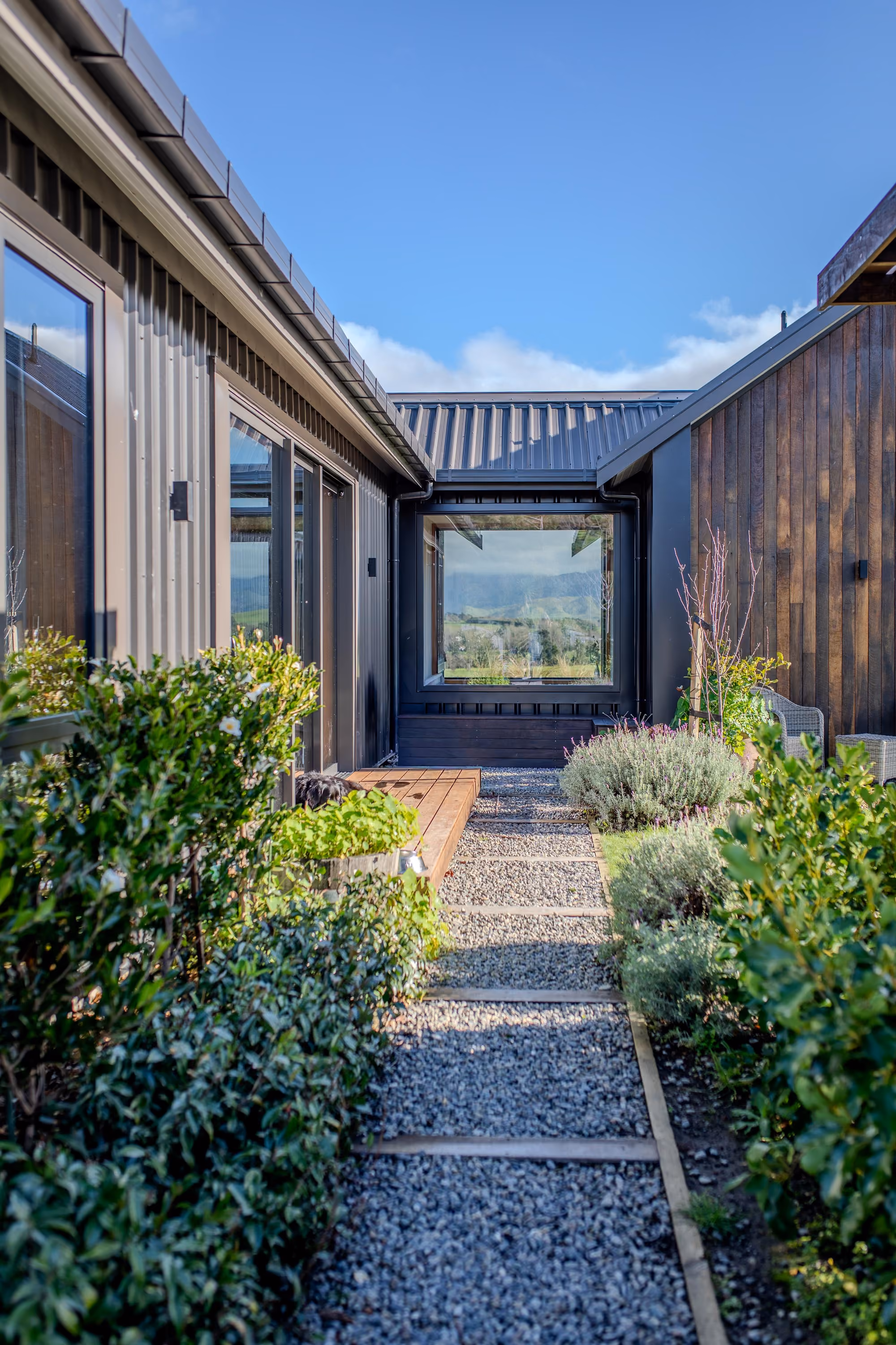 Gravel walkway between wings of the home, lined with hedging and garden beds