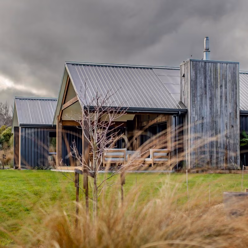 Exterior of the home with corrugated steel roof and board-and-batten cladding, surrounded by tussock grass