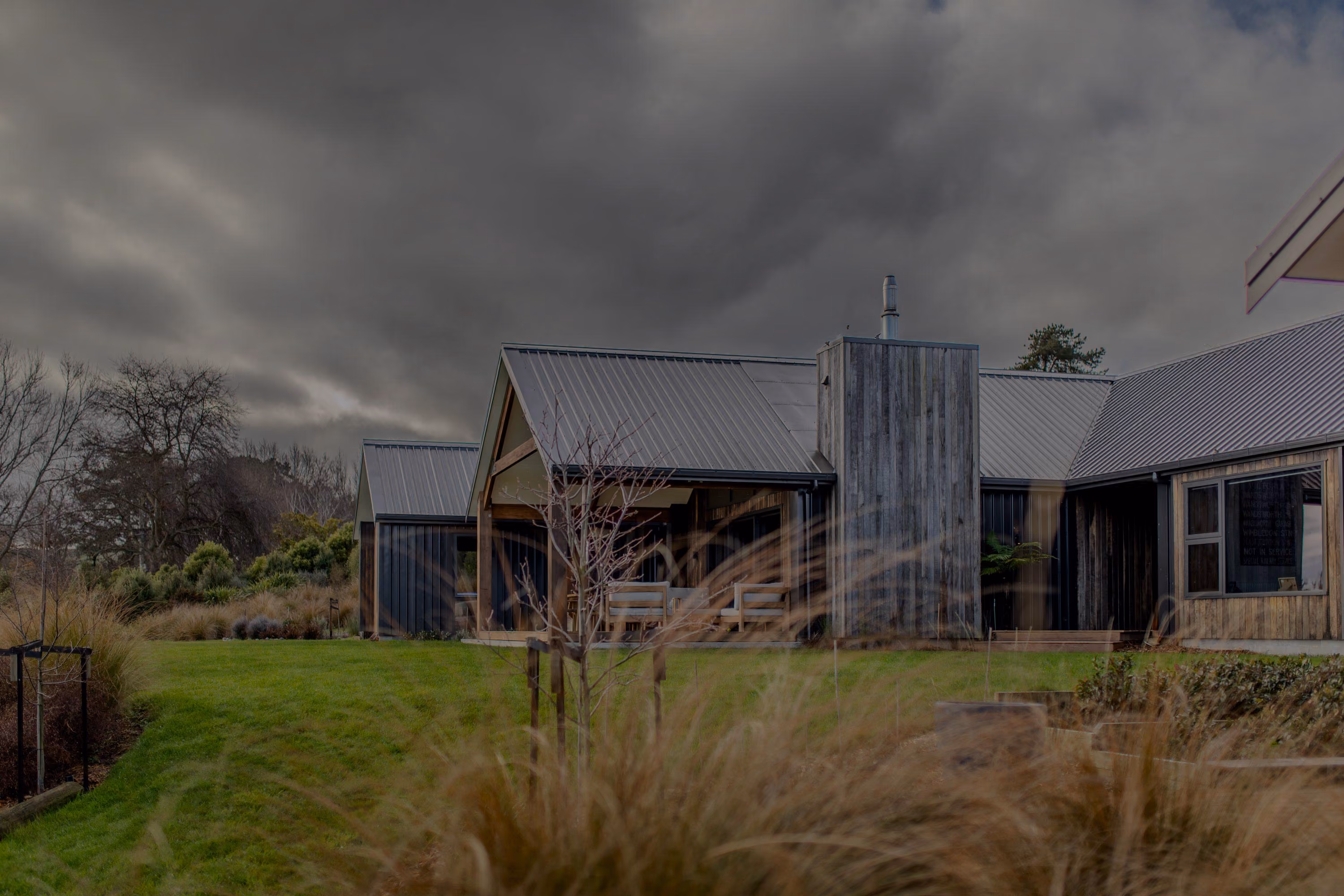 Exterior view of the home under a cloudy sky, showing weatherboard cladding, chimney and lawn