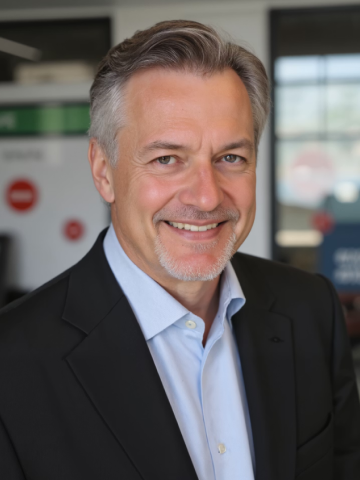 Smiling middle-aged man with gray hair and goatee wearing a black blazer and light blue shirt in an office setting.
