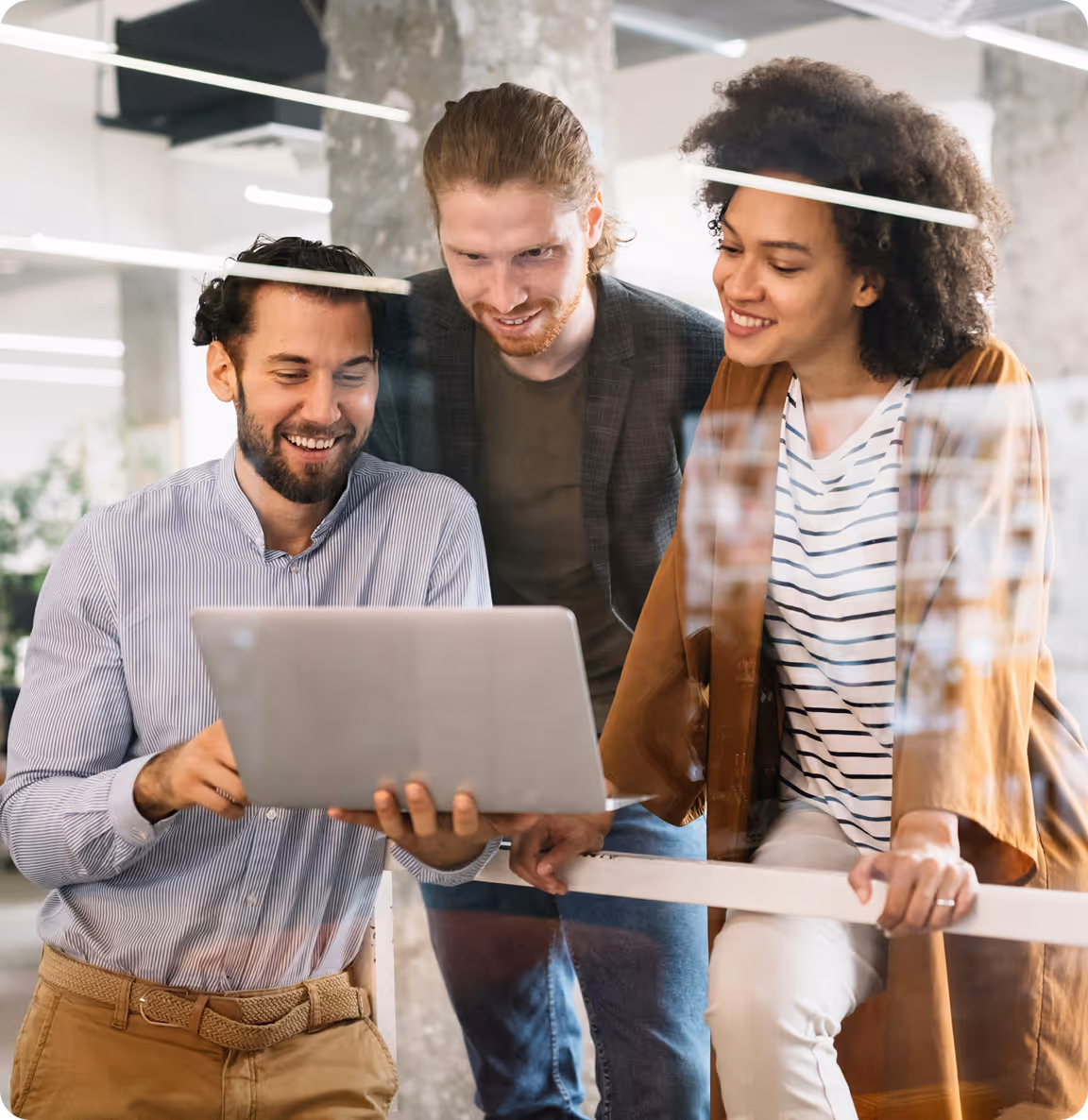 Three diverse colleagues smiling while viewing laptop together in modern office