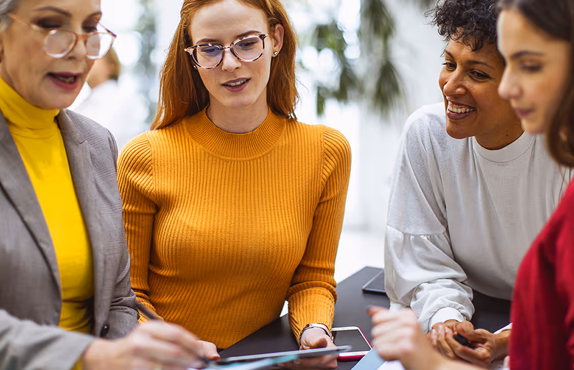 Diverse group of women smiling together while looking at smartphone and tablet devices outdoors