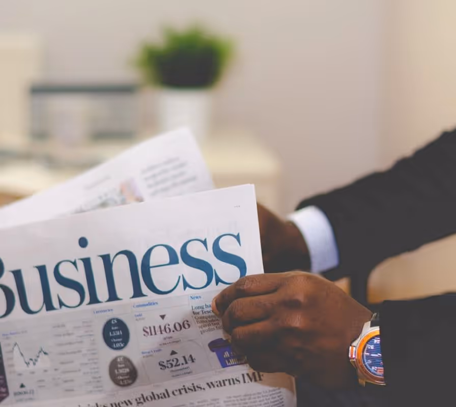 Person in business attire reading newspaper with financial data and stock information visible.