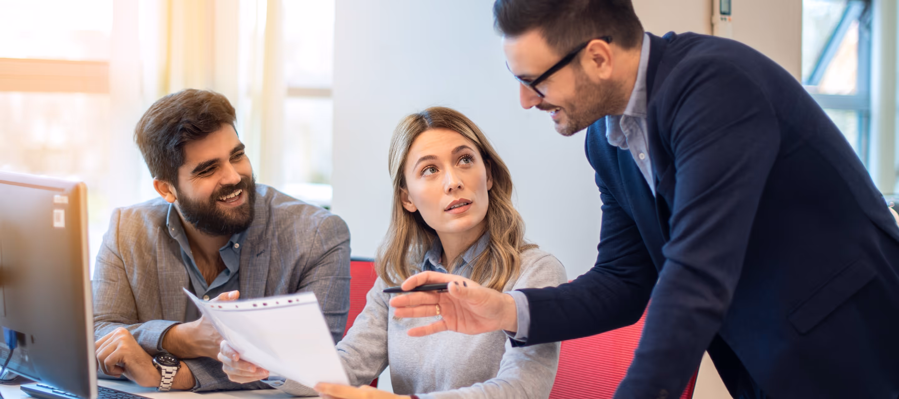 Three business professionals discussing project on tablet in modern office setting