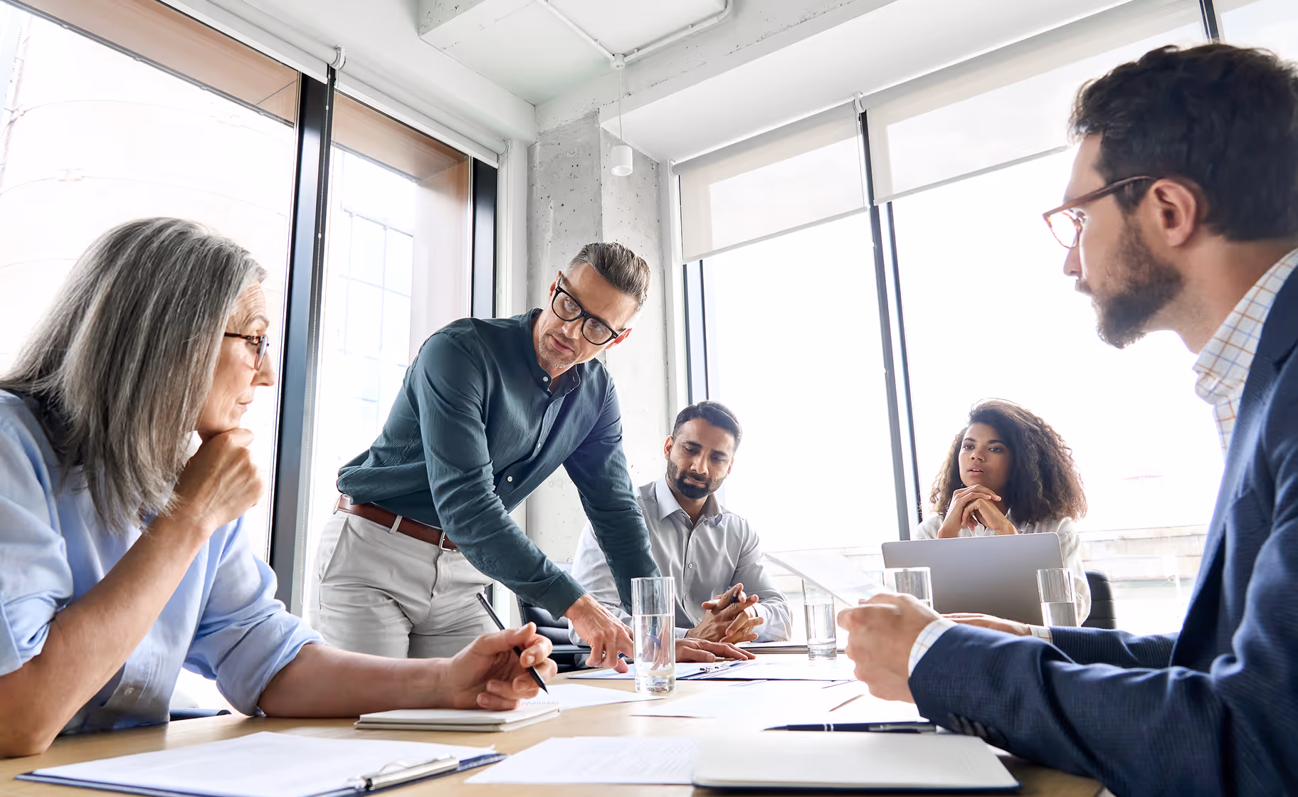 Professional team in modern office boardroom meeting around table with laptops and documents