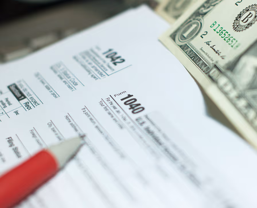 IRS Form 1040 tax document with US dollar bill and red pen nearby