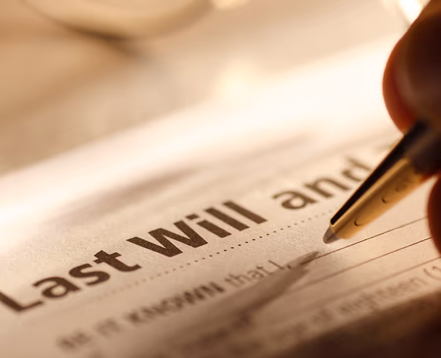 Pen writing "Last will and" on a will document with blurred background