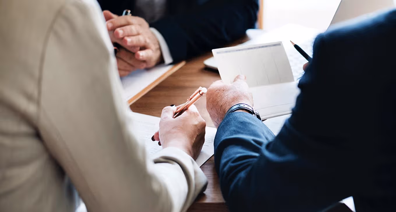 Business professionals reviewing documents and notes during a meeting at wooden table.