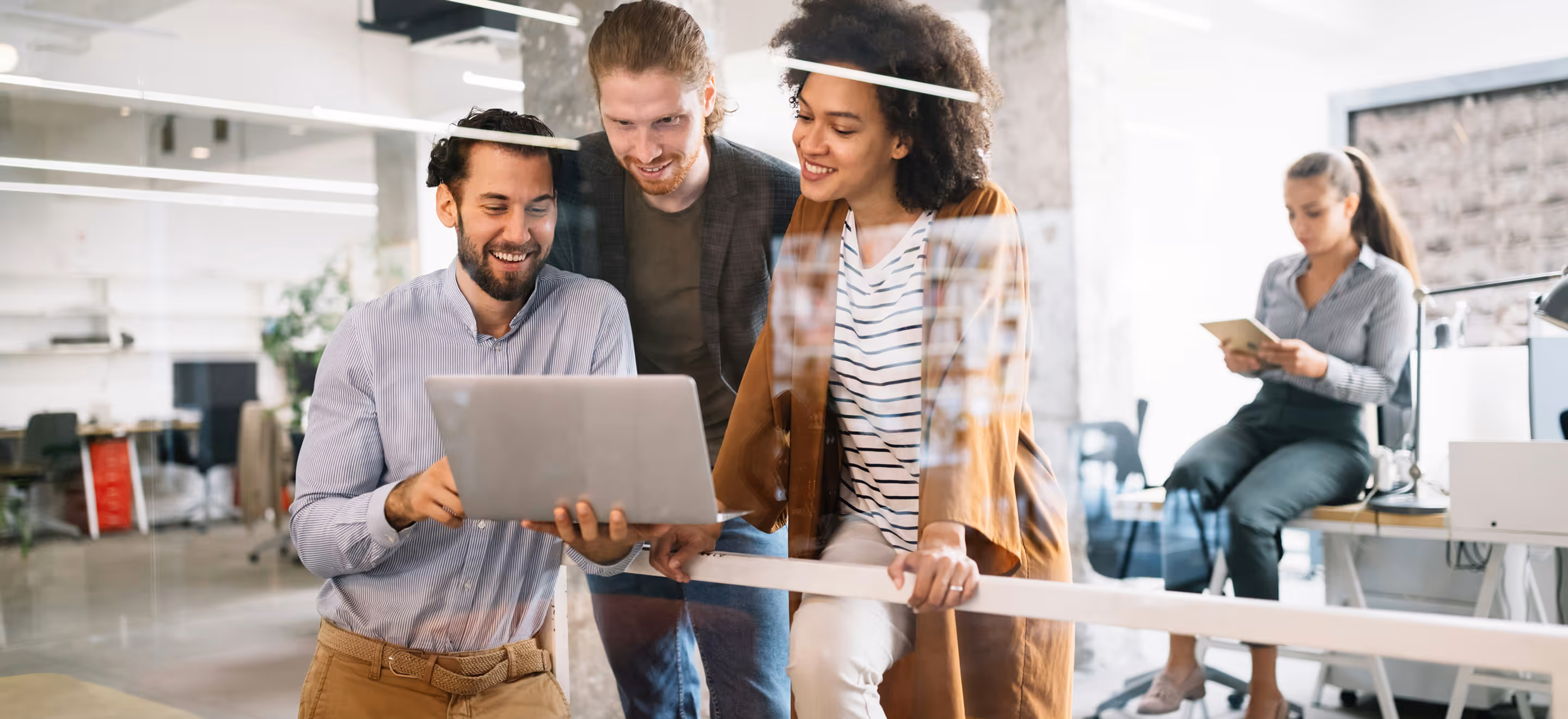 Three happy colleagues gathered around laptop in modern office, viewing content together