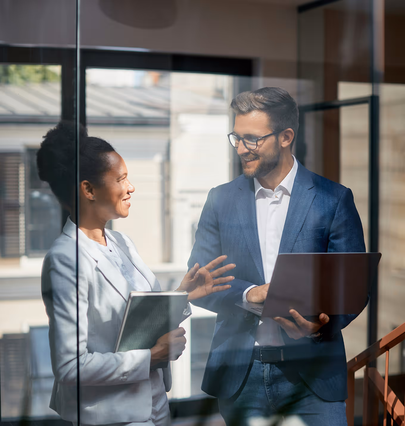 Two business professionals discuss work on laptop in modern office setting.