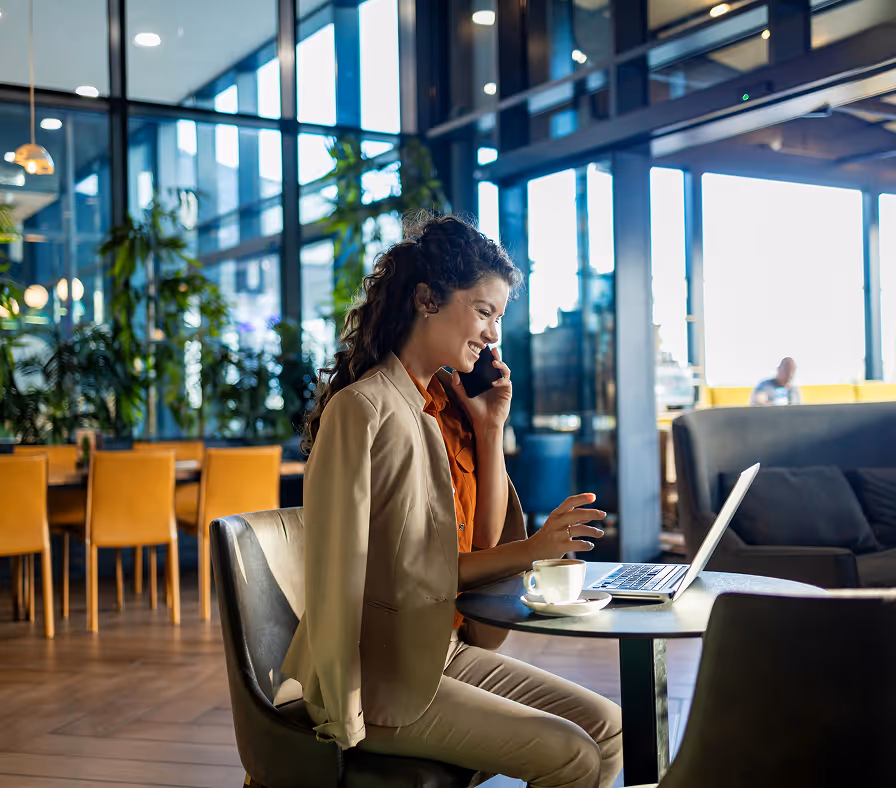 Woman in beige suit on phone at laptop in modern office with yellow chairs