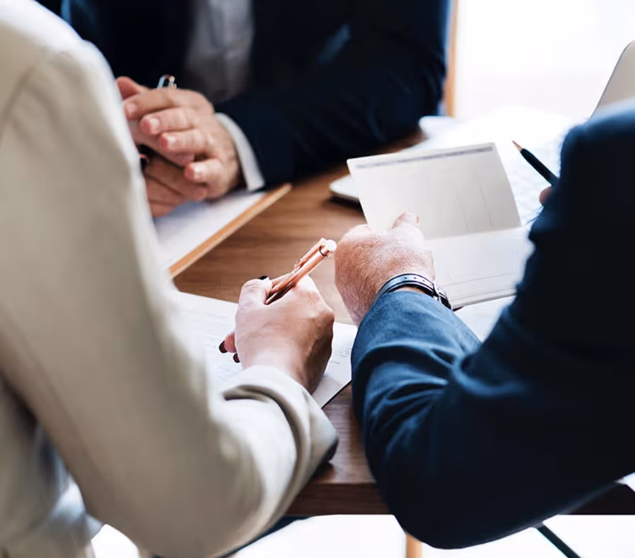 Business professionals discussing documents and signing contract at wooden table.