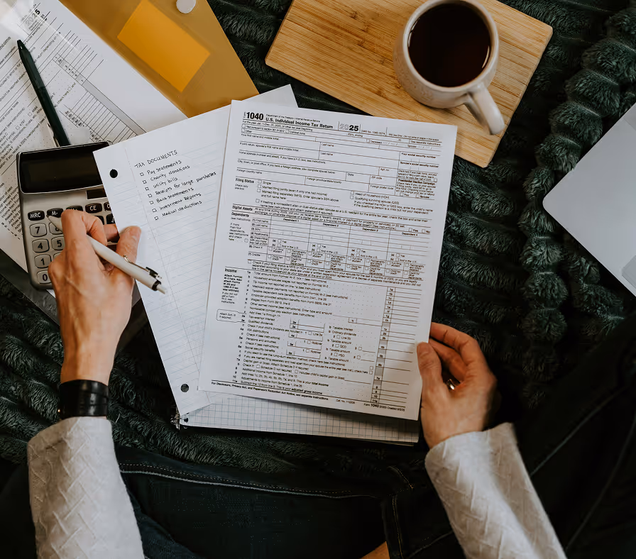 Person completing tax form 1040 with calculator, coffee and documents on desk