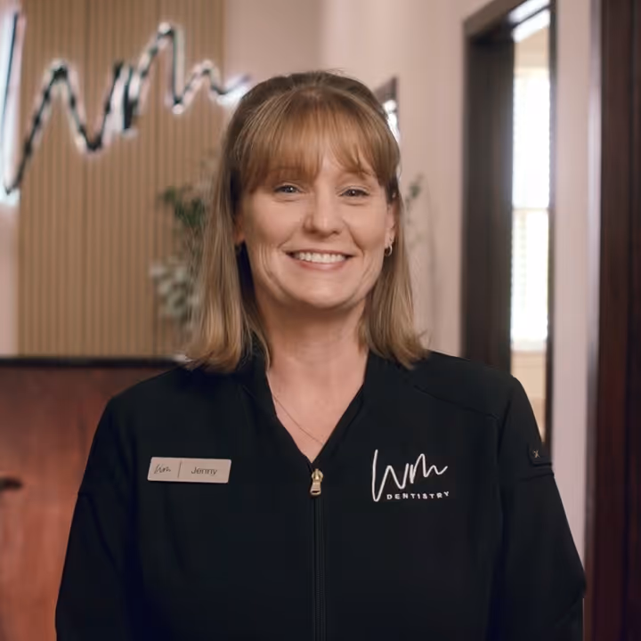 Smiling woman wearing a black jacket with 'WM Dentistry' logo and a name tag that reads Jenny.