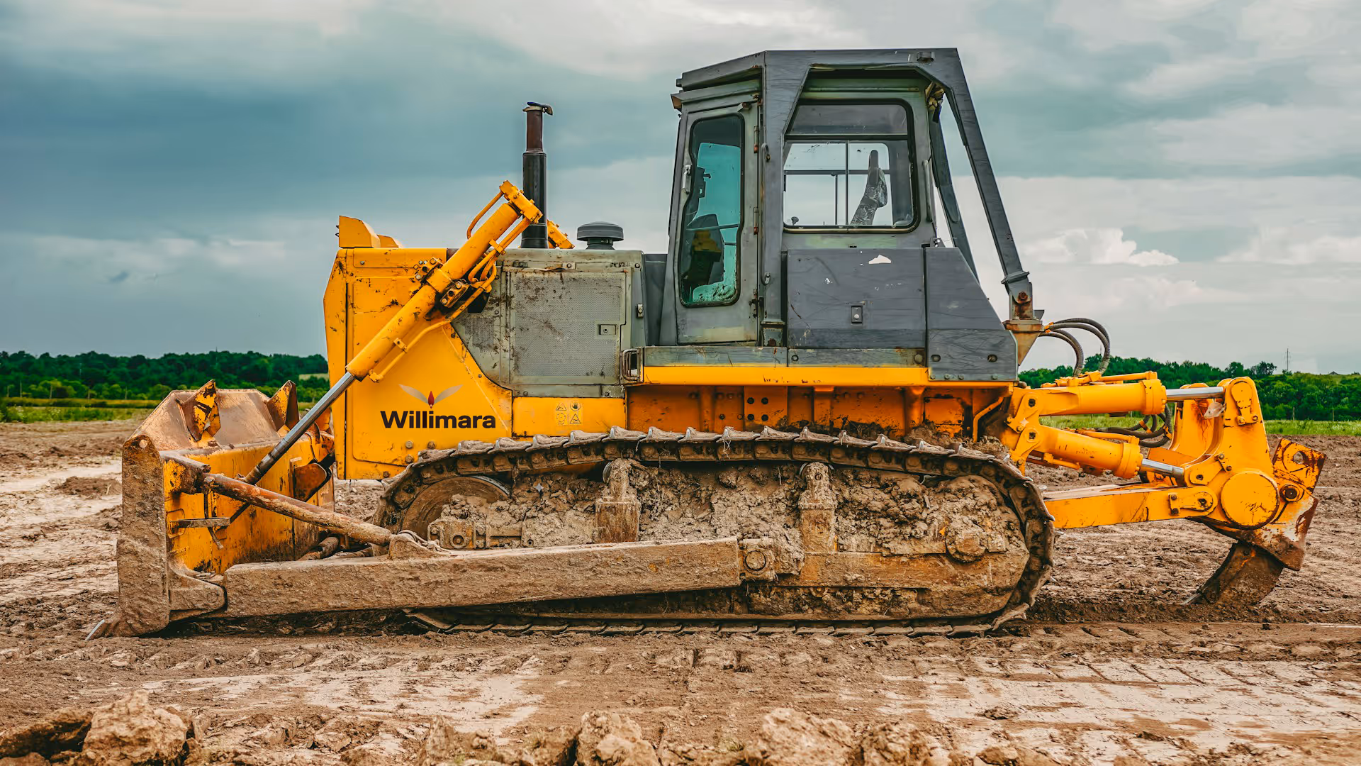 Yellow and gray bulldozer with Willimara logo parked on muddy construction site.