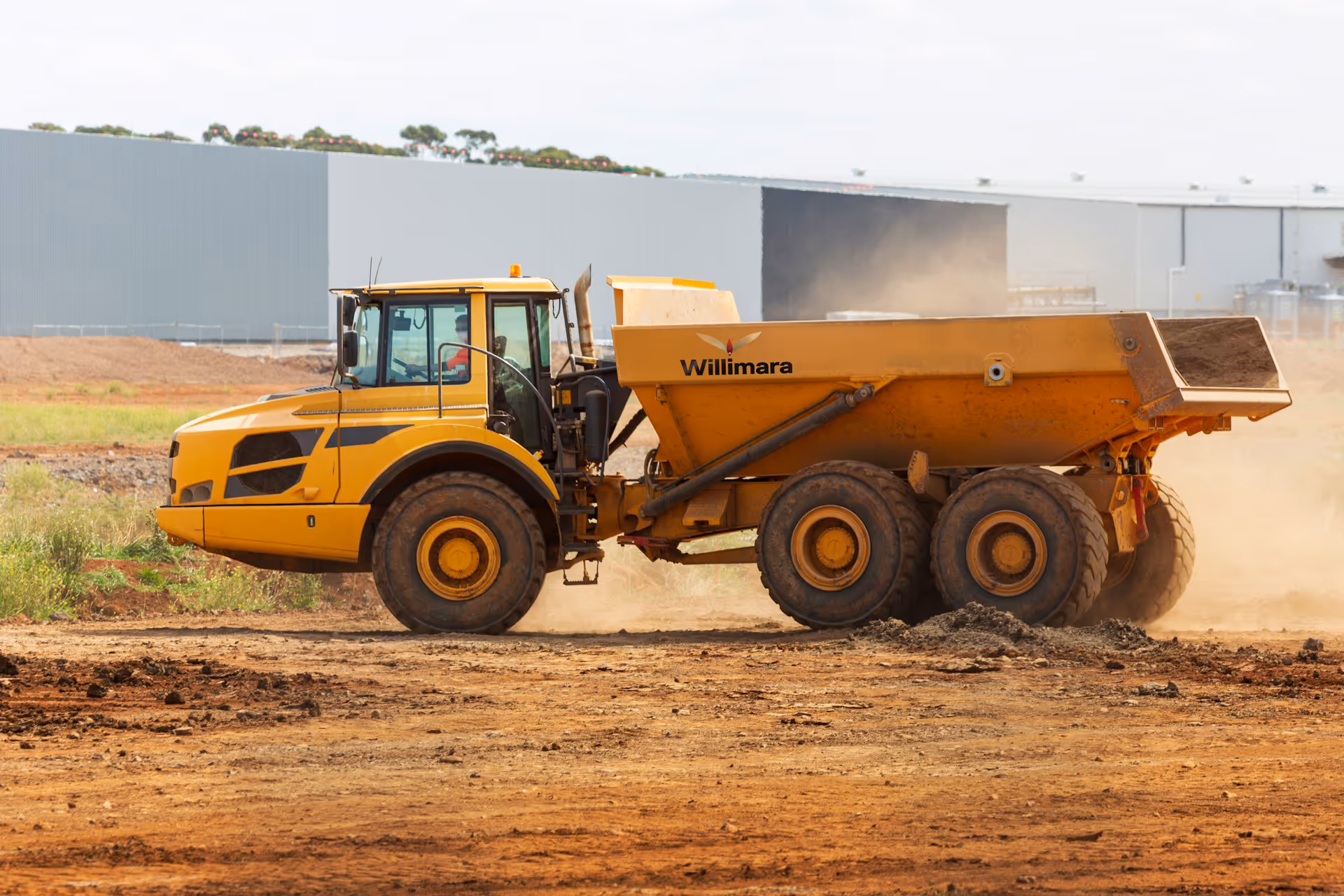 Yellow Willimara dump truck on a dusty construction site with large mud tires.