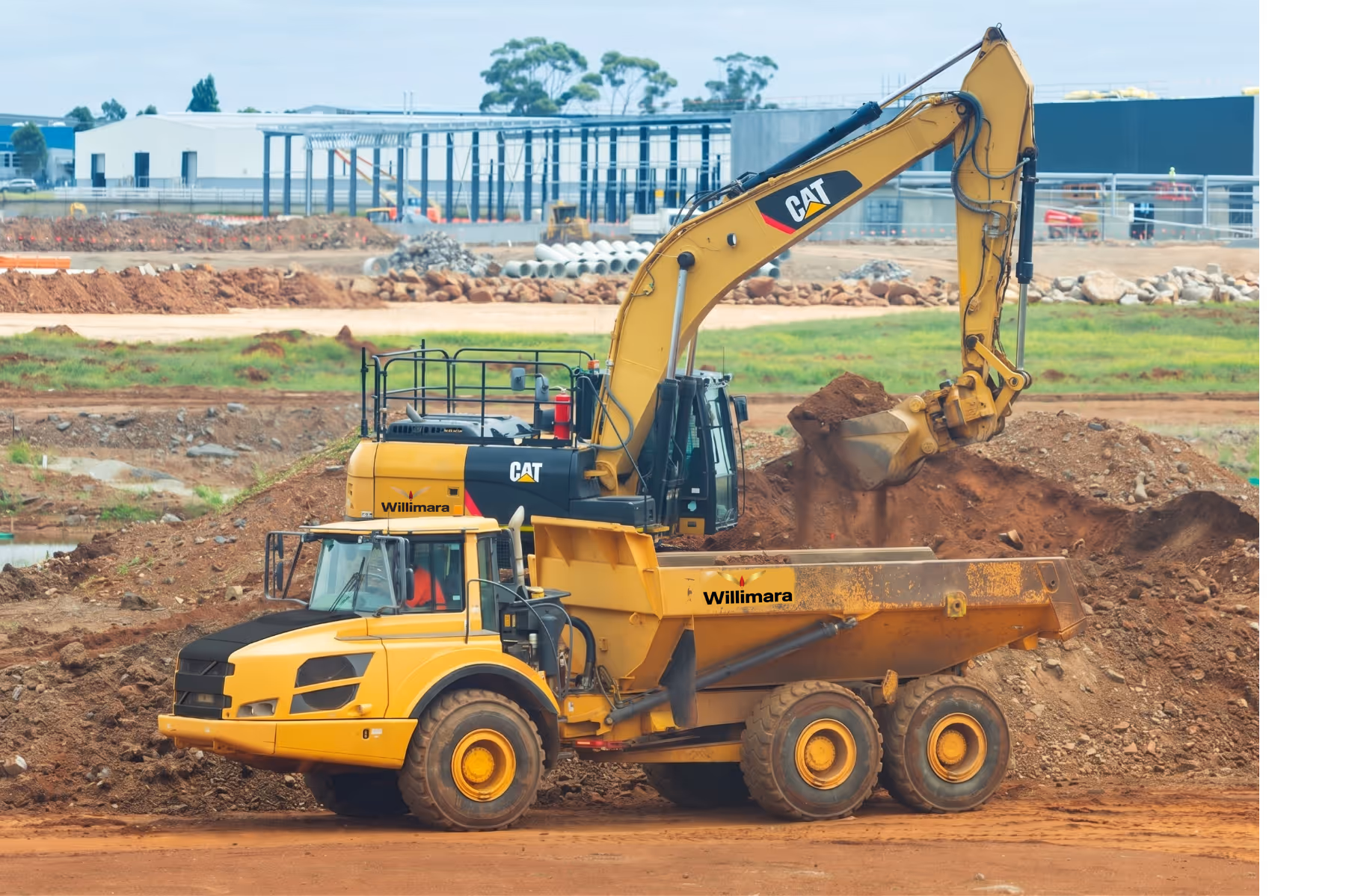 Yellow CAT excavator loading dirt into a yellow Willimara dump truck at a construction site.