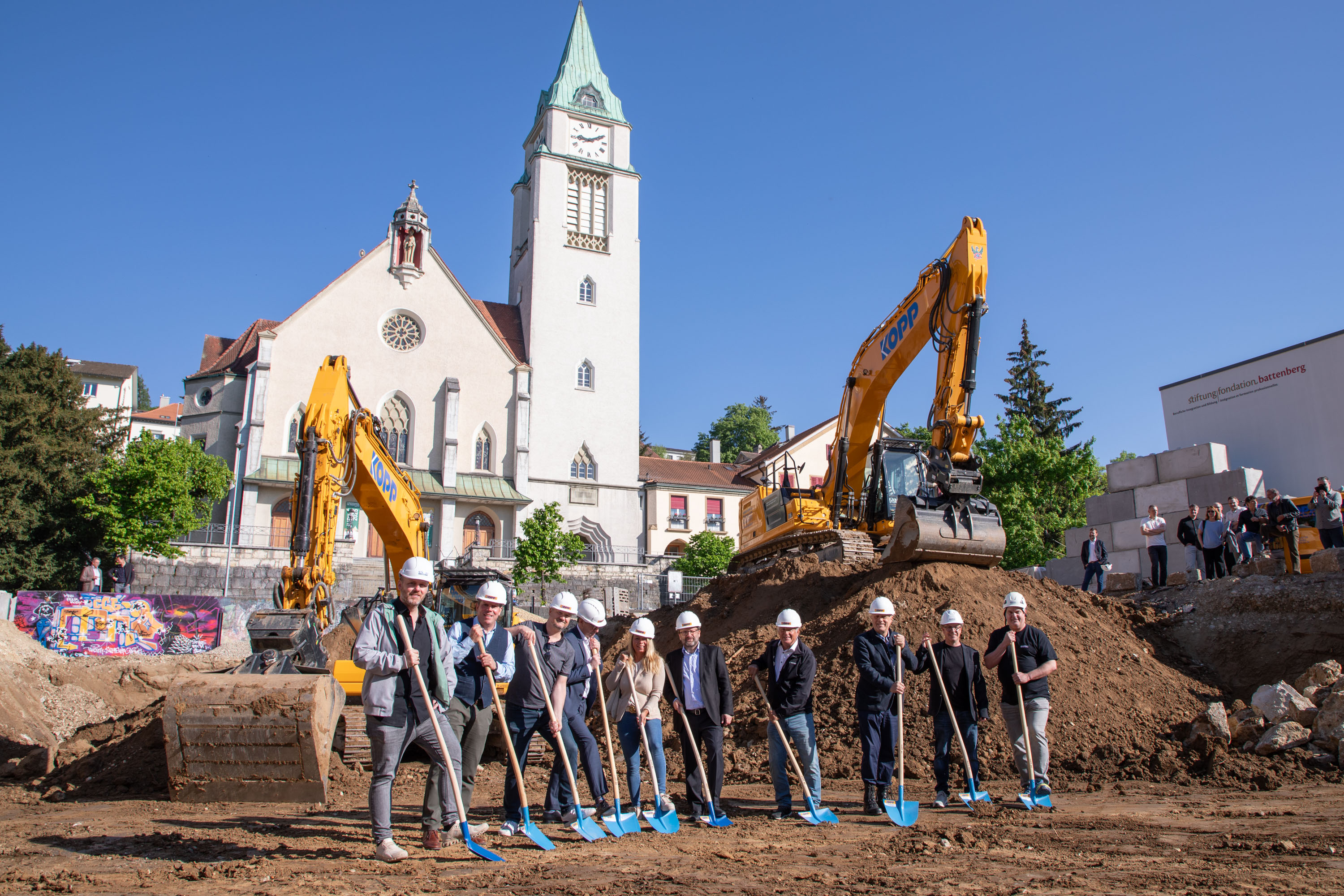 Foto von 15 Personen, die jeweils ein Diplom vor einem weißen Zelt im Freien halten.