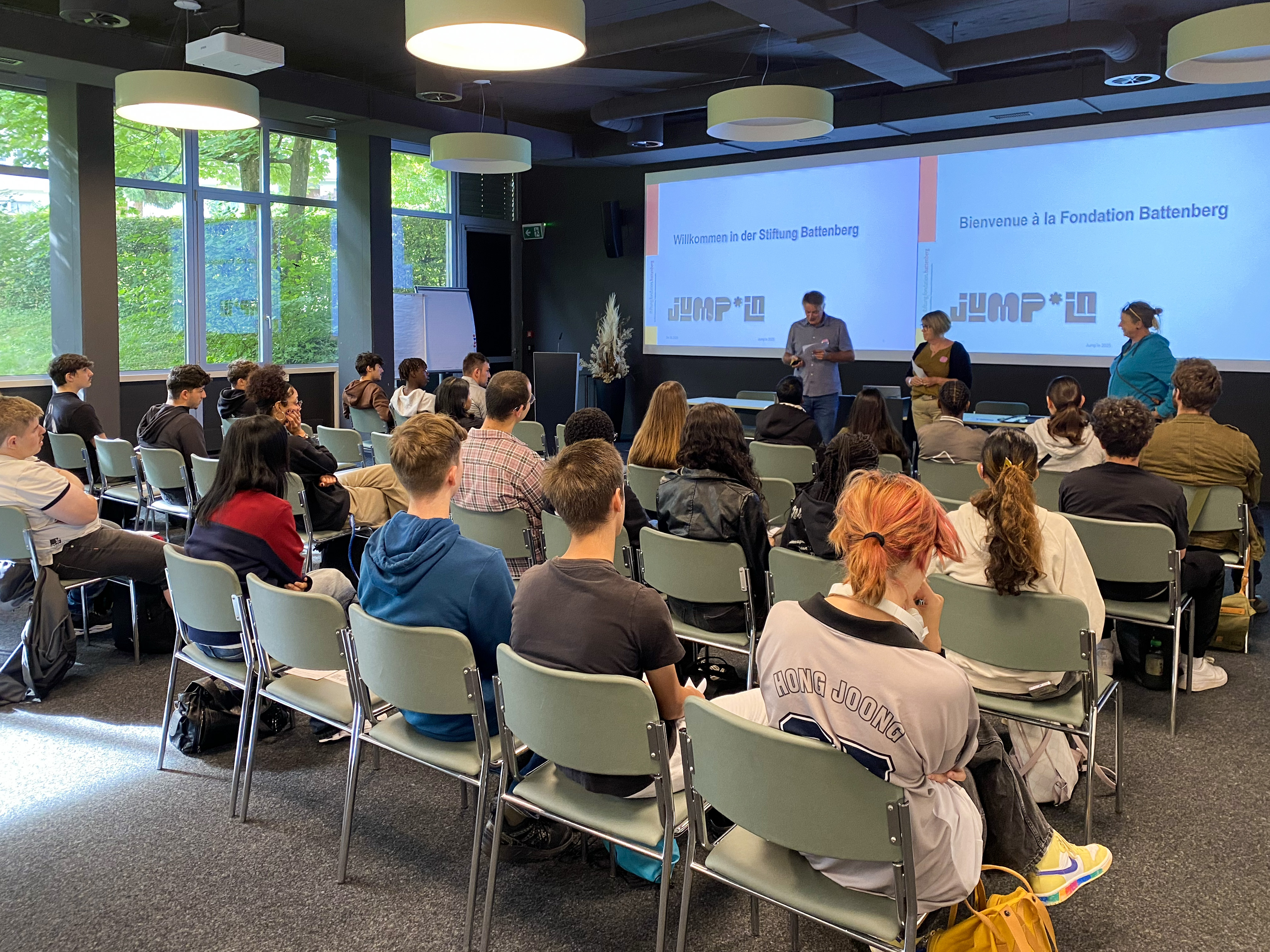 Foto von 15 Personen, die jeweils ein Diplom vor einem weißen Zelt im Freien halten.