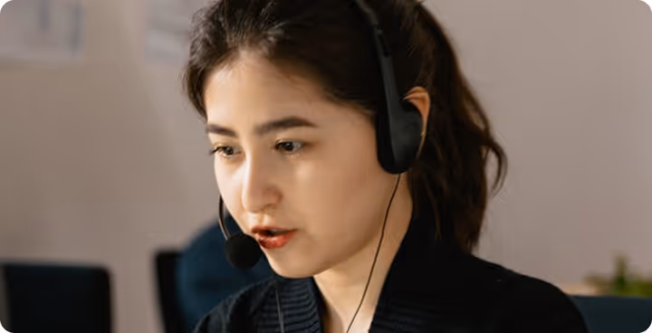 Young woman with dark hair wearing a headset with microphone, engaged in conversation.