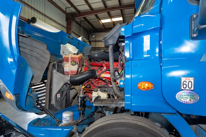 Coolant service for a heavy-duty truck, showing the open hood, engine, coolant reservoir, hoses, and cooling system components.