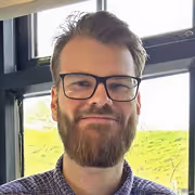 Bearded man wearing glasses and striped shirt indoors near window