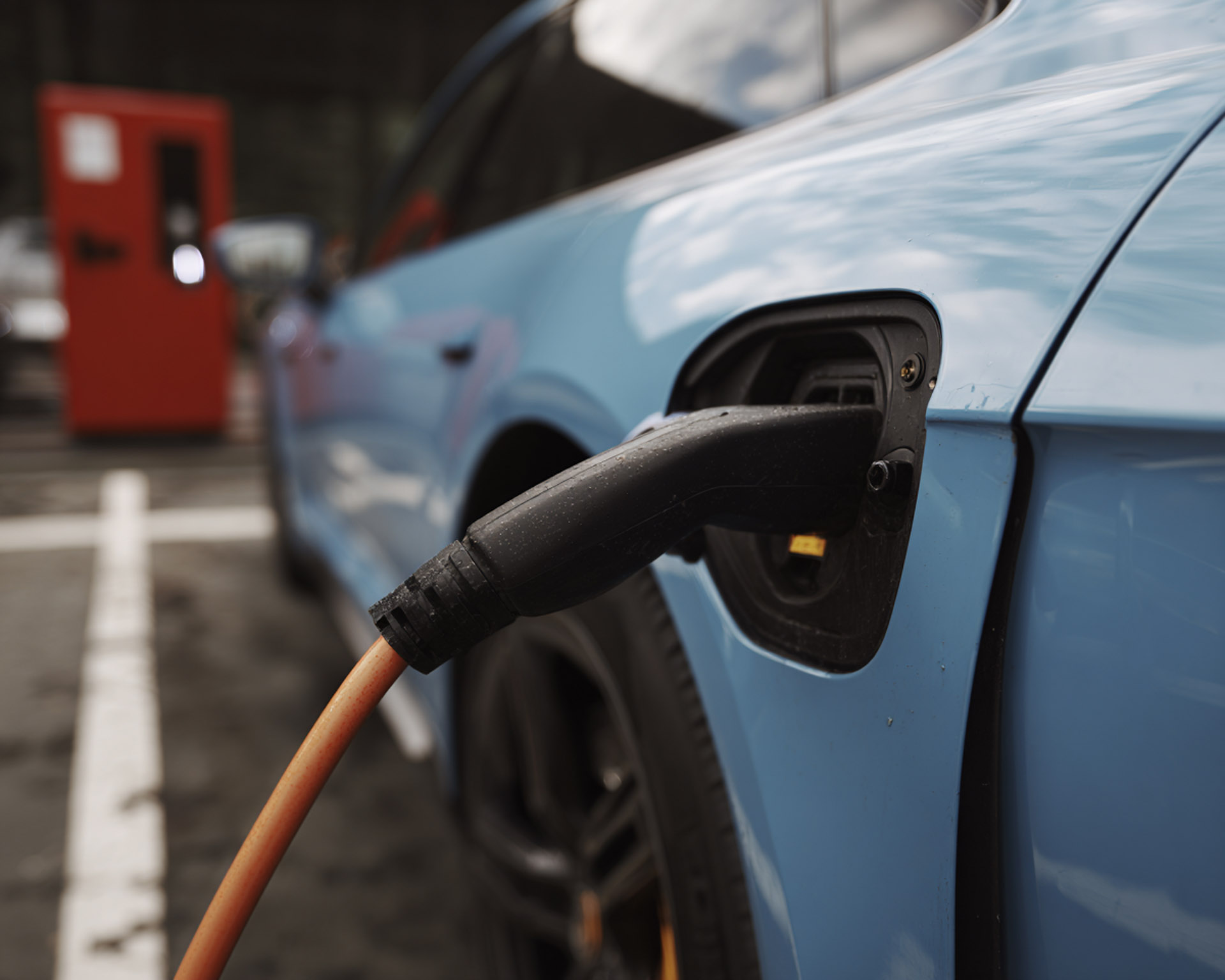 Close-up of a blue electric car charging with a plugged-in charging cable.