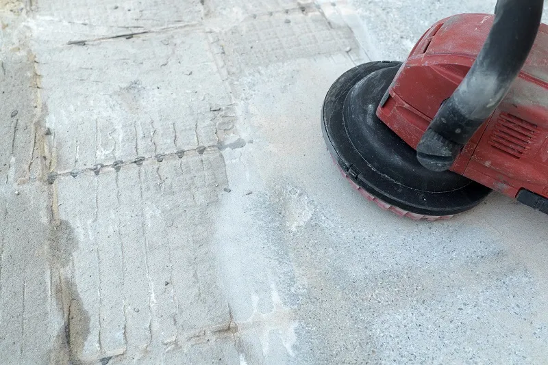 Red power floor grinder or sander smoothing a concrete surface with visible abrasion marks.