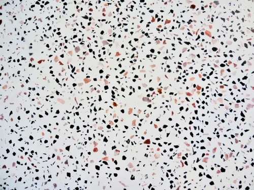 Close-up of terrazzo surface with scattered black, pink, and reddish stone chips on a white background.