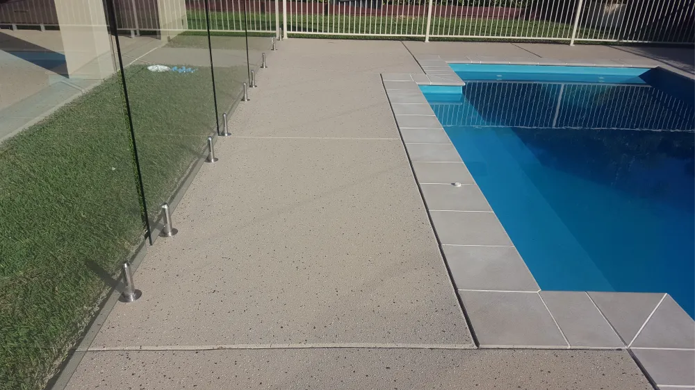 Anti-slip concrete surrounding a pool, with glass safety fence and clear blue water in the swimming pool.