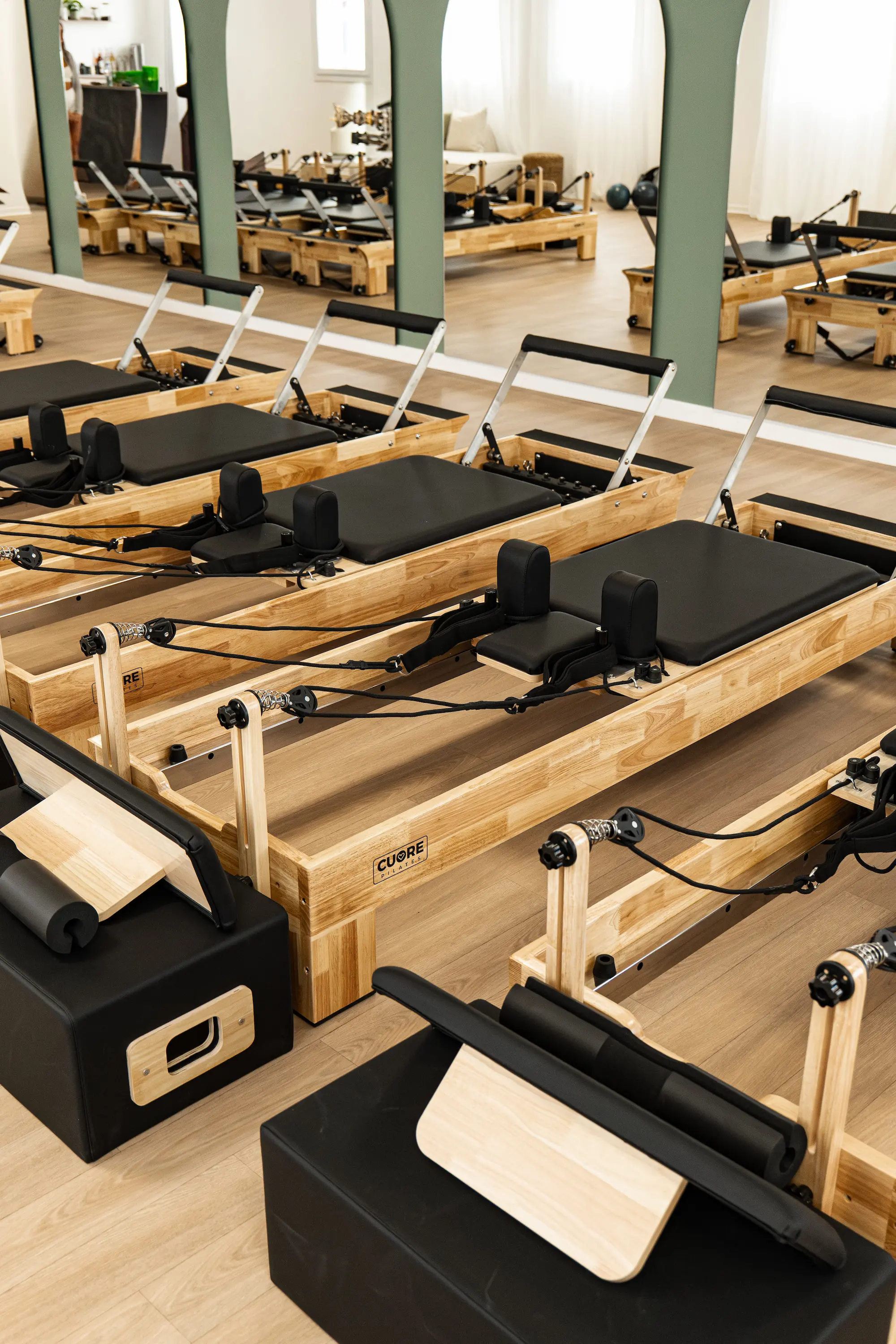 Appareils de Pilates en bois avec surfaces rembourrées noires disposés dans une salle lumineuse avec miroir.