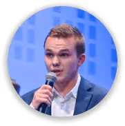 Jeune homme en costume bleu parlant dans un micro sur un fond bleu.