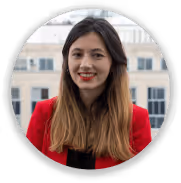 Portrait d'une femme souriante aux cheveux longs portant un blazer rouge devant un bâtiment.