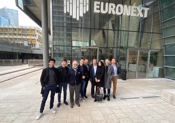 Groupe de huit personnes posant devant le bâtiment de la bourse Euronext avec façade vitrée.