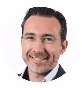 Portrait d'un homme souriant portant des lunettes avec des cheveux foncés coiffés en arrière.