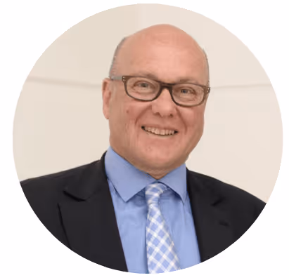 Homme souriant portant des lunettes, un costume noir, une chemise bleue et une cravate à motif bleu clair.