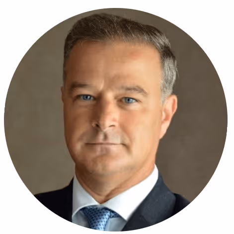 Portrait d'un homme en costume gris avec chemise blanche et cravate bleue, fond neutre.