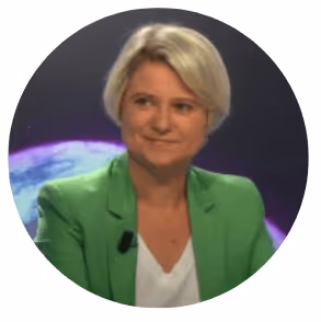 Femme aux cheveux courts blonds en veste verte souriant devant un fond sombre circulaire.
