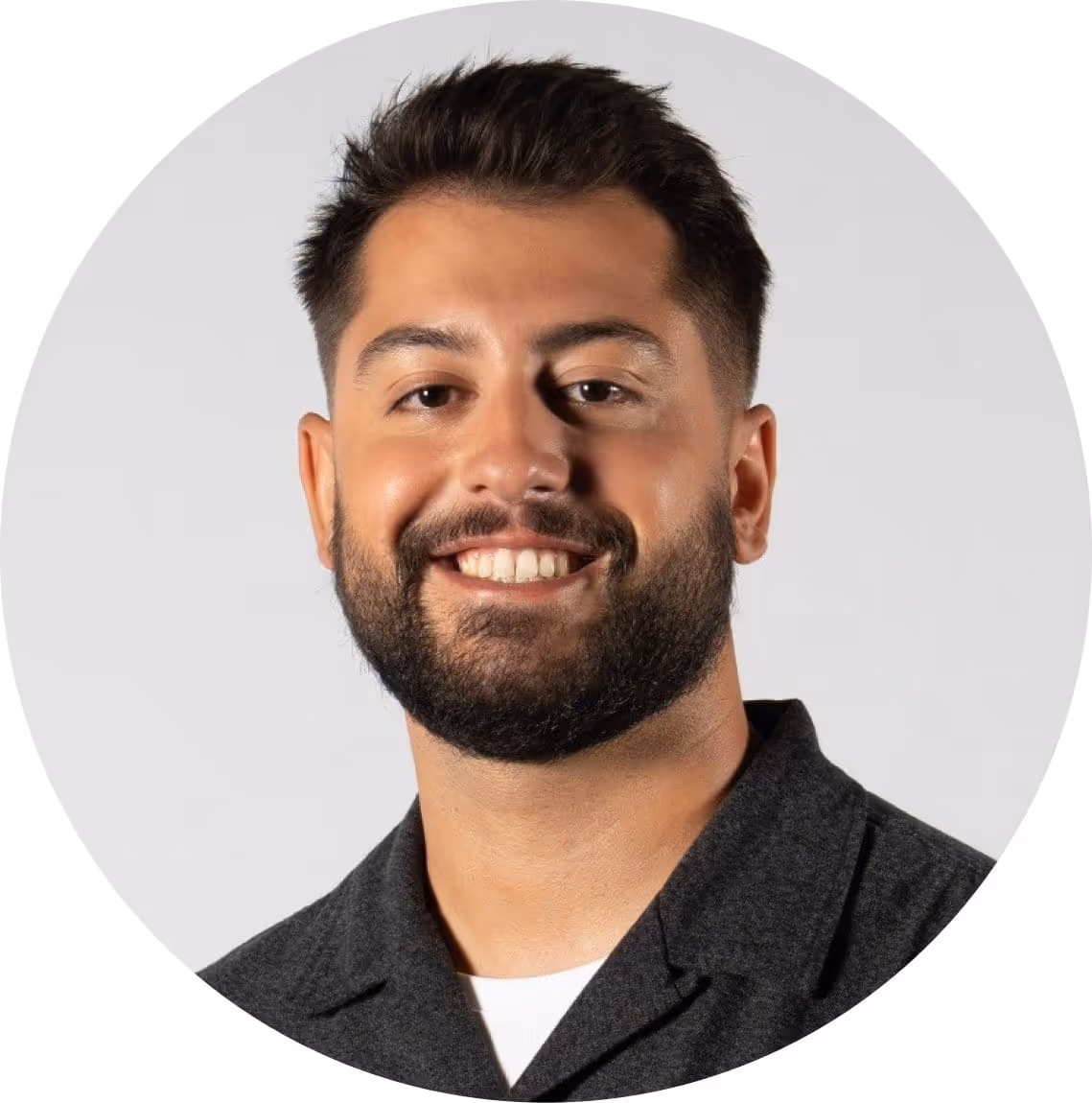 Portrait d'un homme souriant avec barbe et cheveux courts, portant une veste foncée.