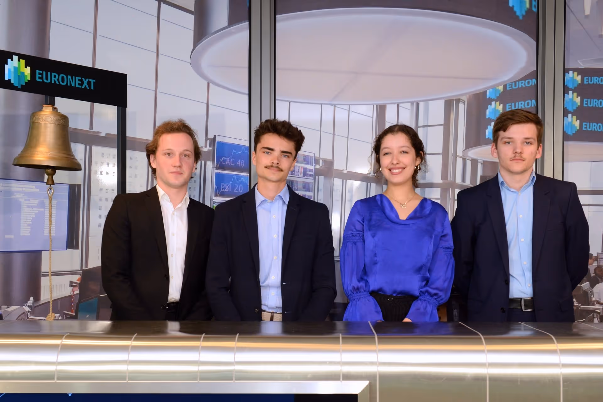 Quatre jeunes professionnels en tenue formelle posent derrière un comptoir dans une salle Euronext.